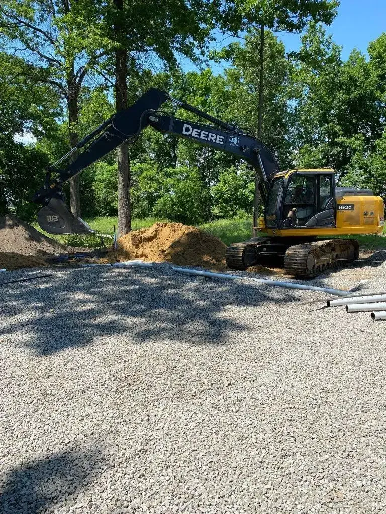 Yellow excavator digging dirt beside a gravel driveway in a wooded area