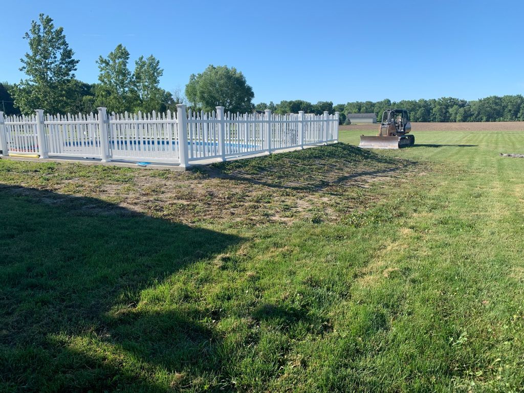 White fenced cemetery on a grassy hill with trees and a headstone in the distance
