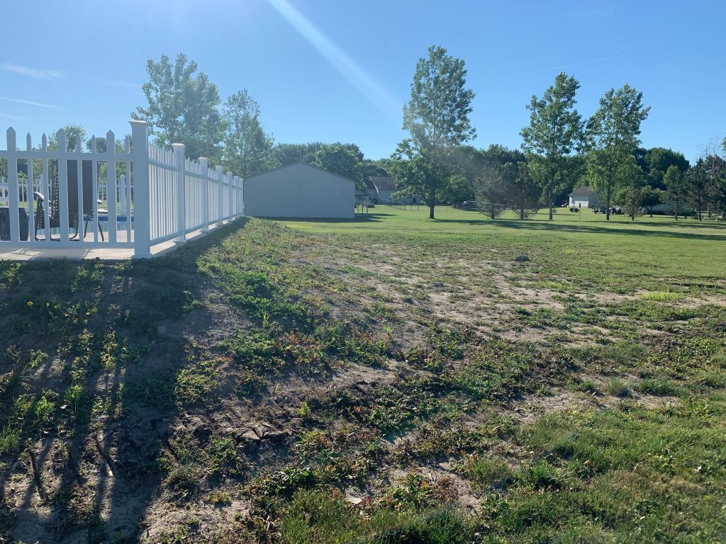Sunny backyard with white fence, small shed, and grassy yard under clear blue sky