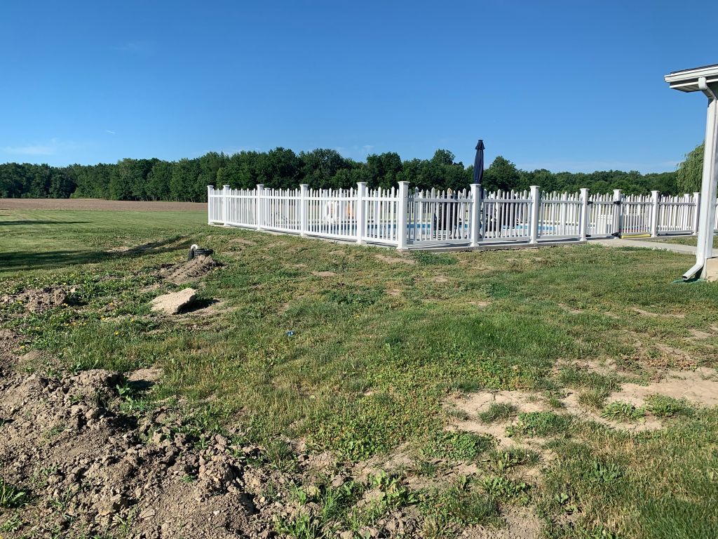 White cemetery fence and grave markers on a grassy hill under a clear blue sky