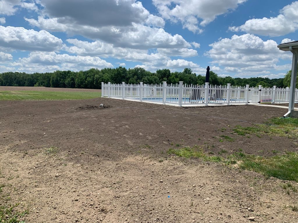 Brown field beside a white fence and open gate under a cloudy blue sky