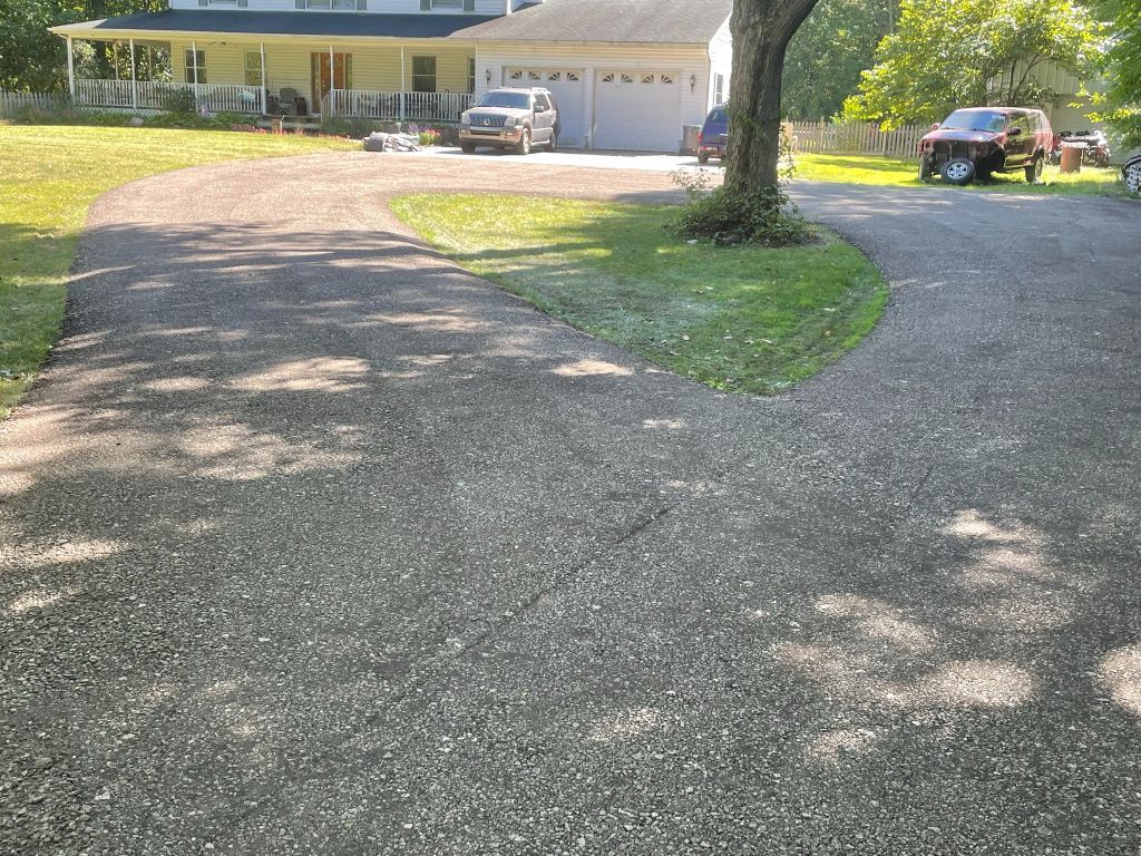 Gravel driveway curving to a house with a white garage and parked vehicles in bright sunlight.