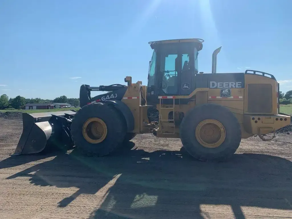 Yellow John Deere loader with a front bucket parked on a gravel lot under a clear sky.