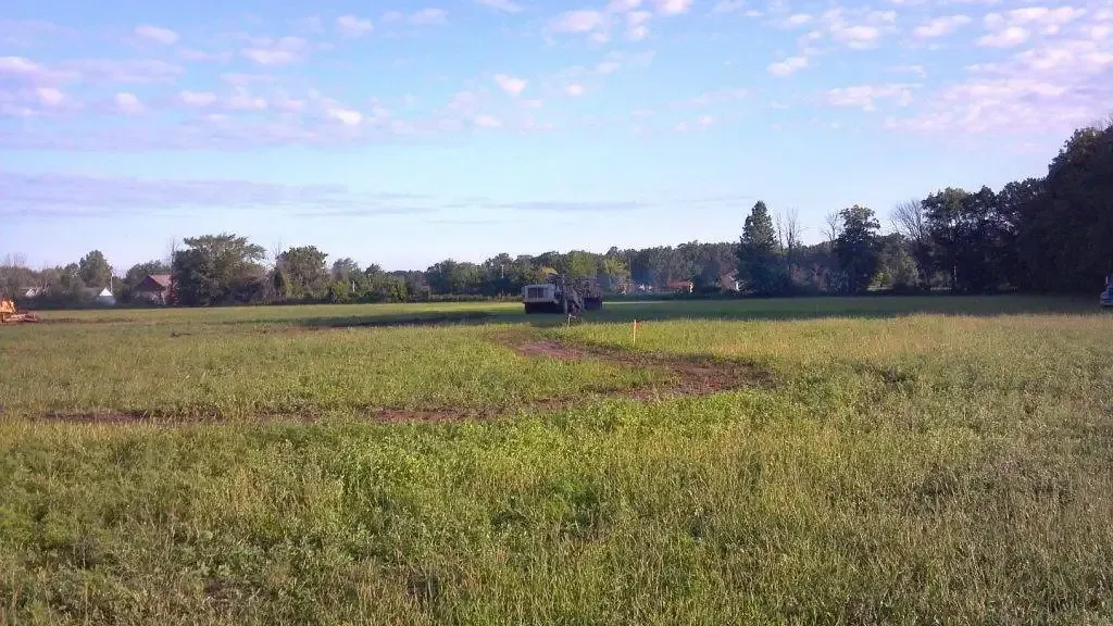 Wide grassy field with a small tractor in the distance under a bright blue sky