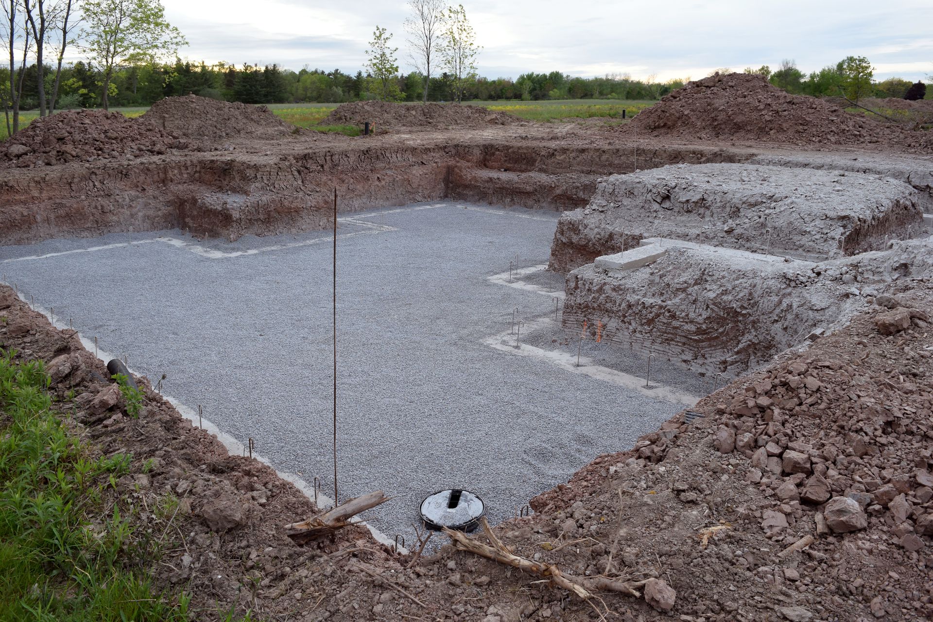 Gravel-lined excavation pit in an open field with dirt mounds around it