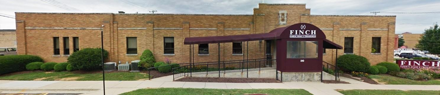 Brick building with a maroon awning and sign, seen from the front on a quiet street.