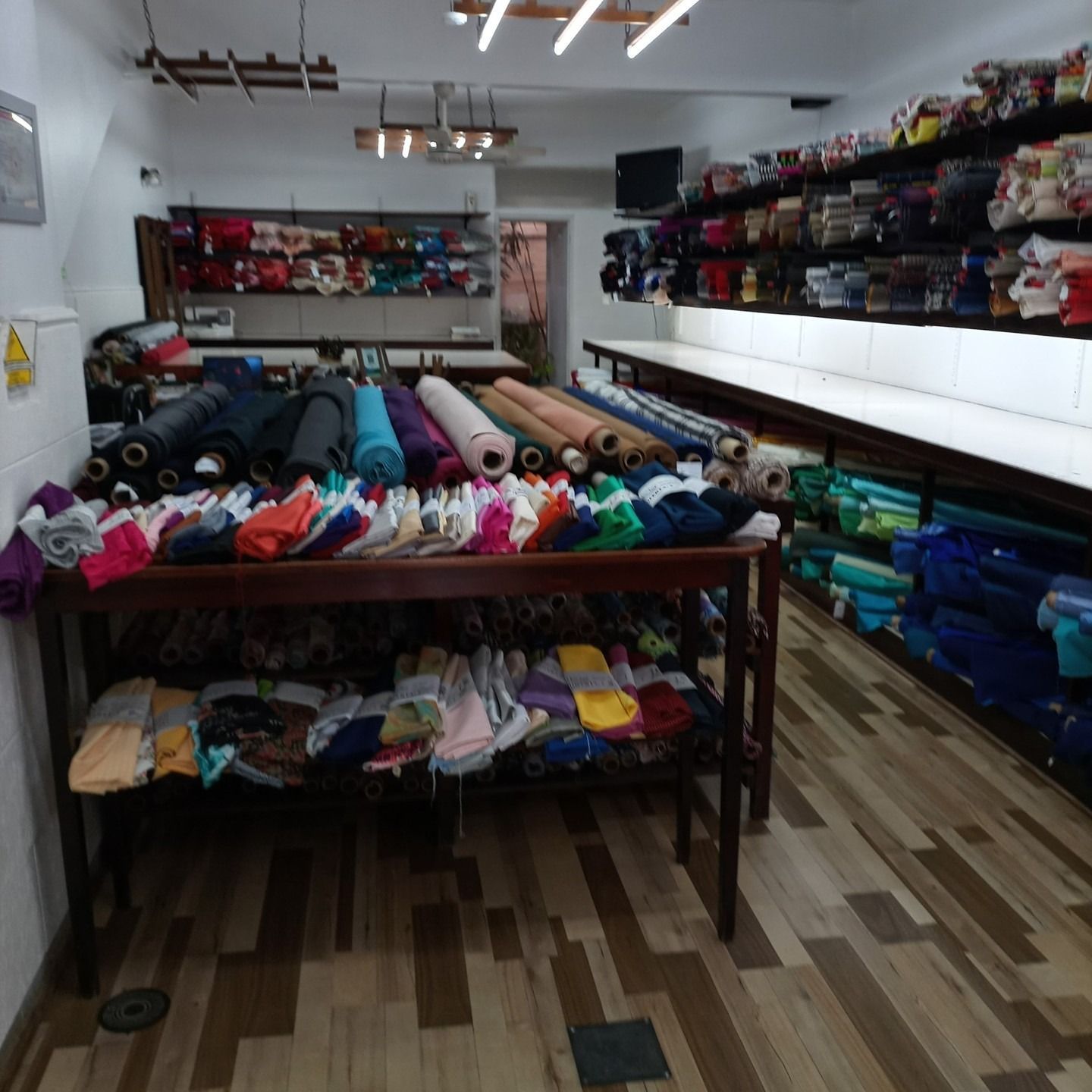 Una tienda de telas con estantes llenos de rollos de colores y telas dobladas sobre una mesa de madera