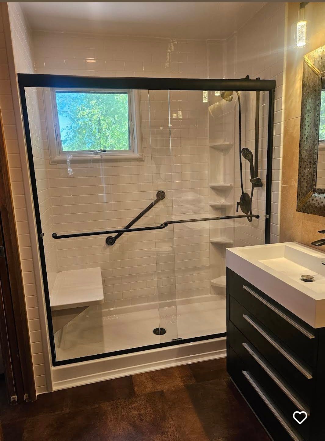 Bathroom with glass walk-in shower, tiled walls, small window, and dark vanity beside it.