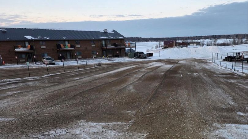 A gravel-covered lot in front of a multi-story brick building, with snow covering the surrounding landscape at dusk.