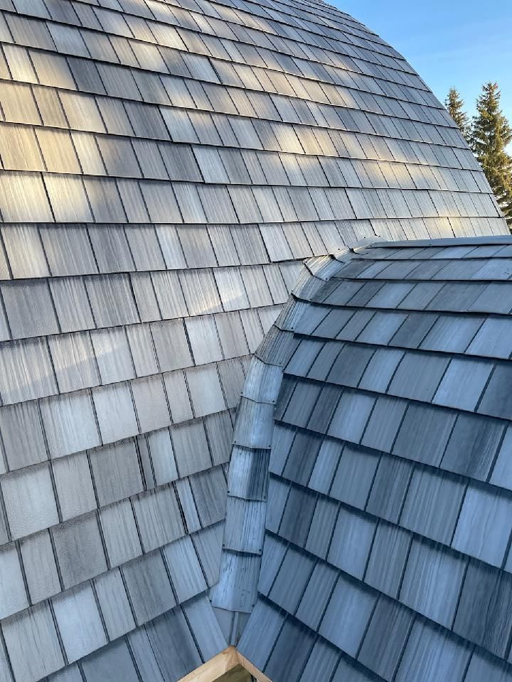 Curved shingled roof with gray wooden tiles under a clear sky, viewed close up.