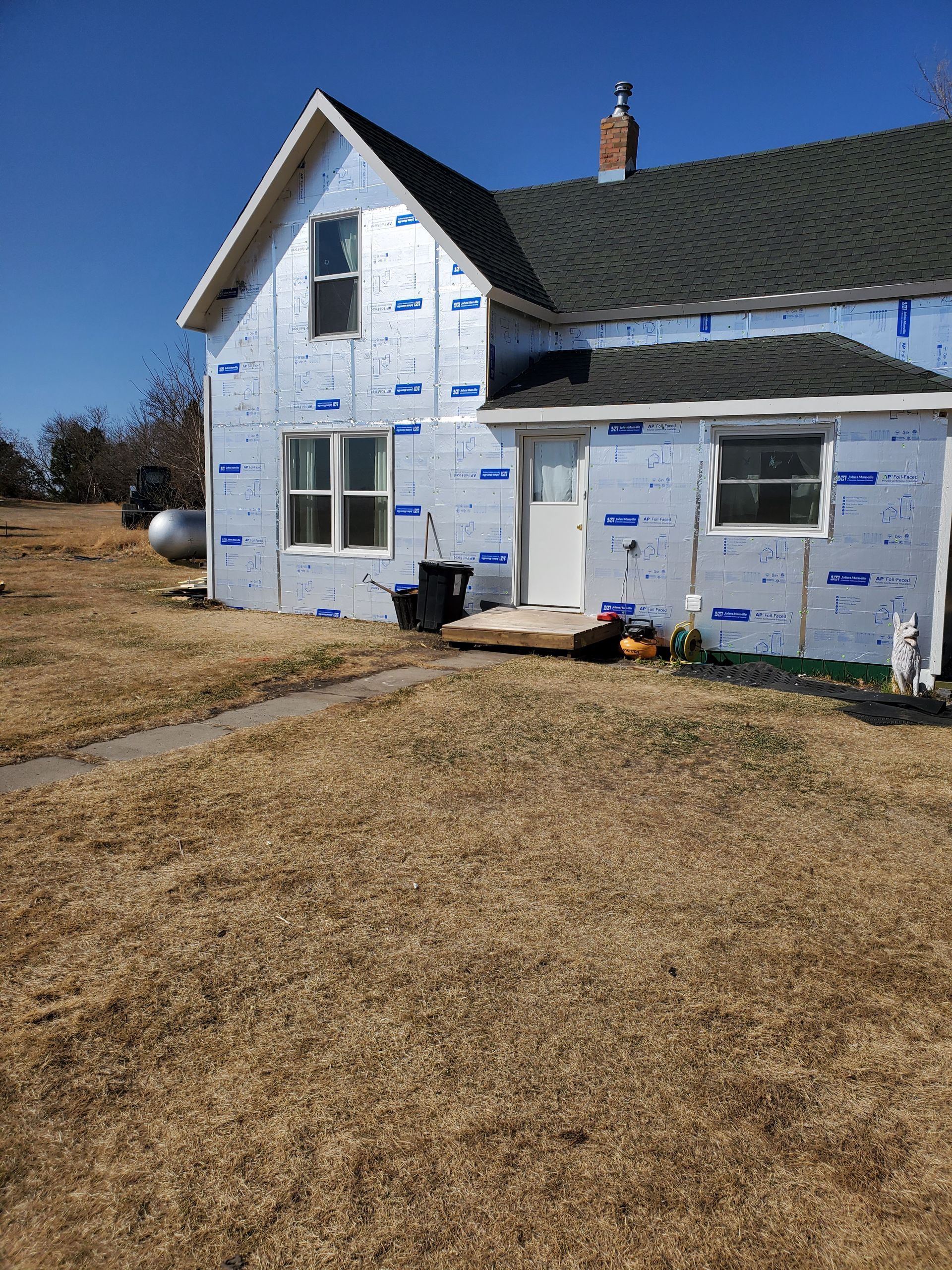 Partially renovated house with white wrap and blue tape under a clear blue sky