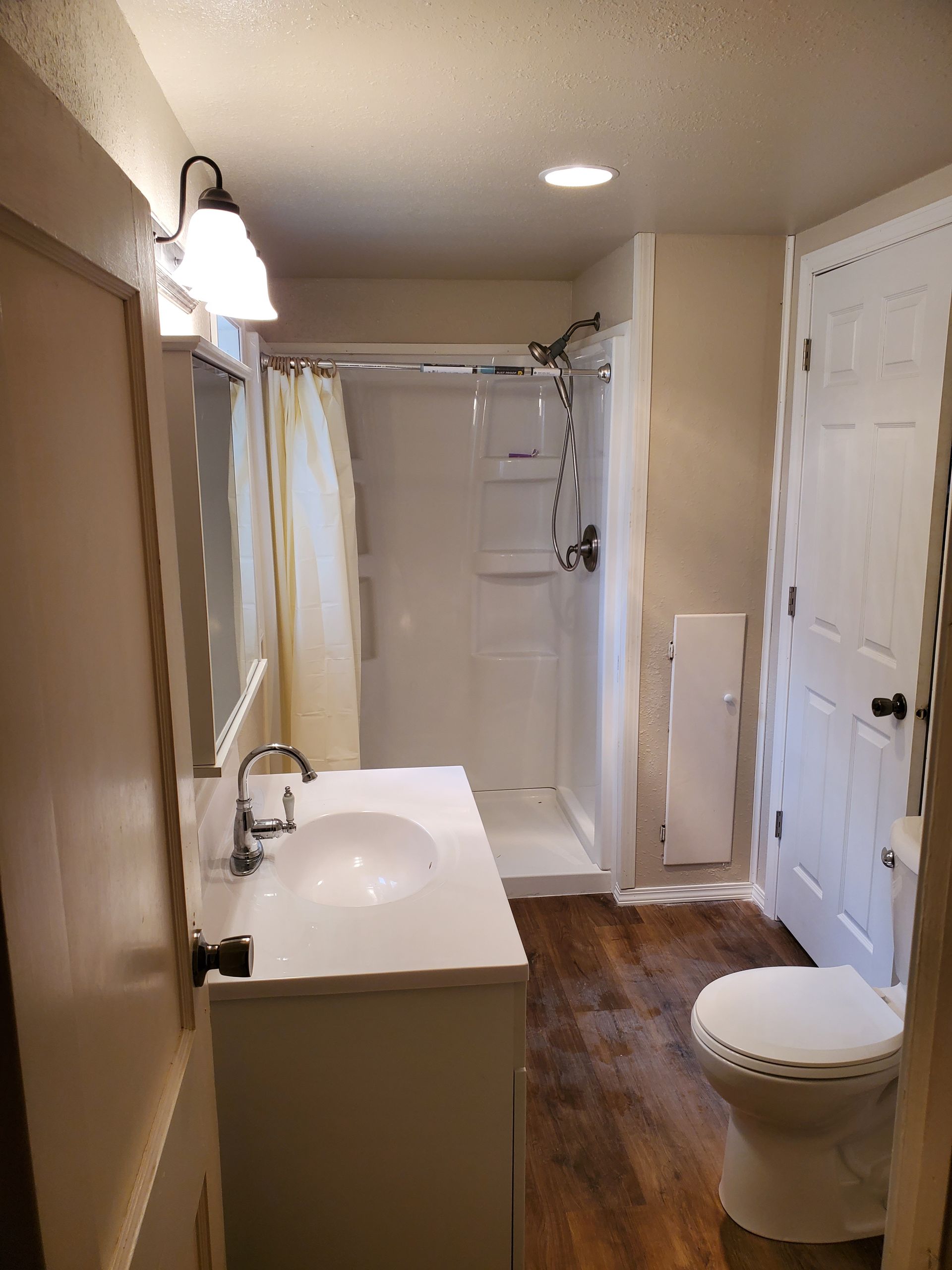 Narrow bathroom with vanity sink, toilet, and shower/tub under warm lighting.