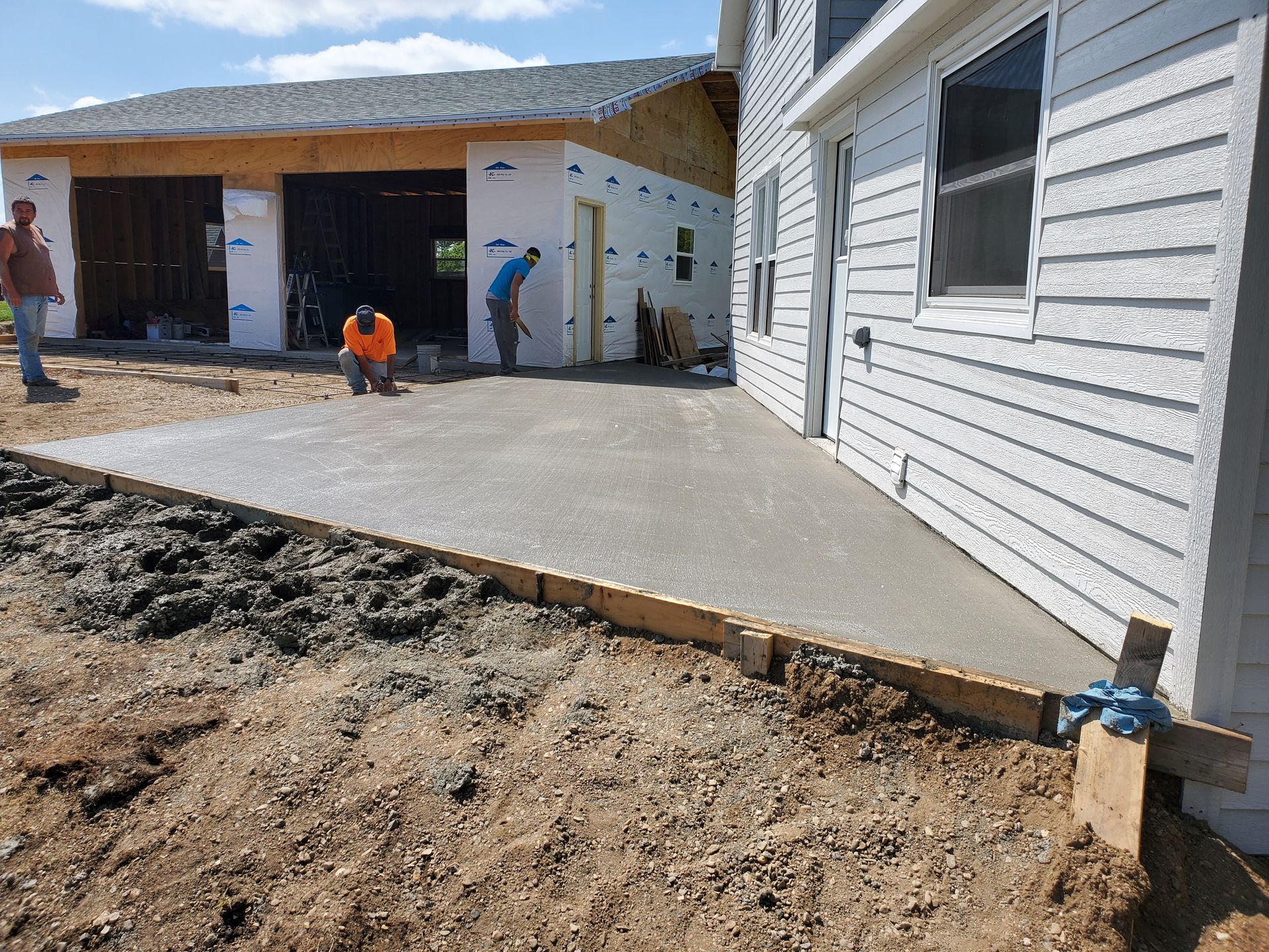 Workers pouring a concrete driveway beside a white house under construction