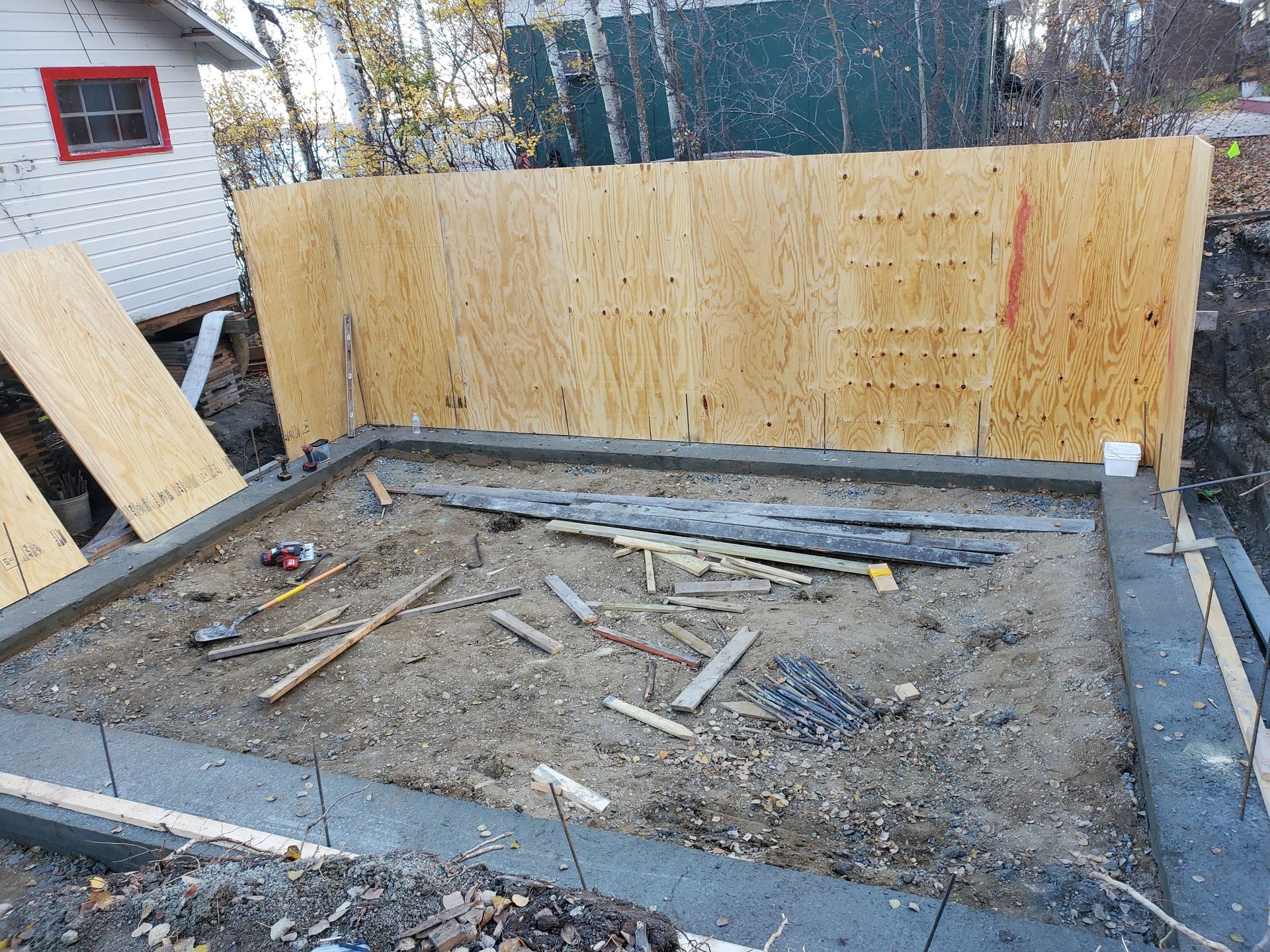 Construction site foundation framed with plywood, gravel floor, and scattered wooden boards