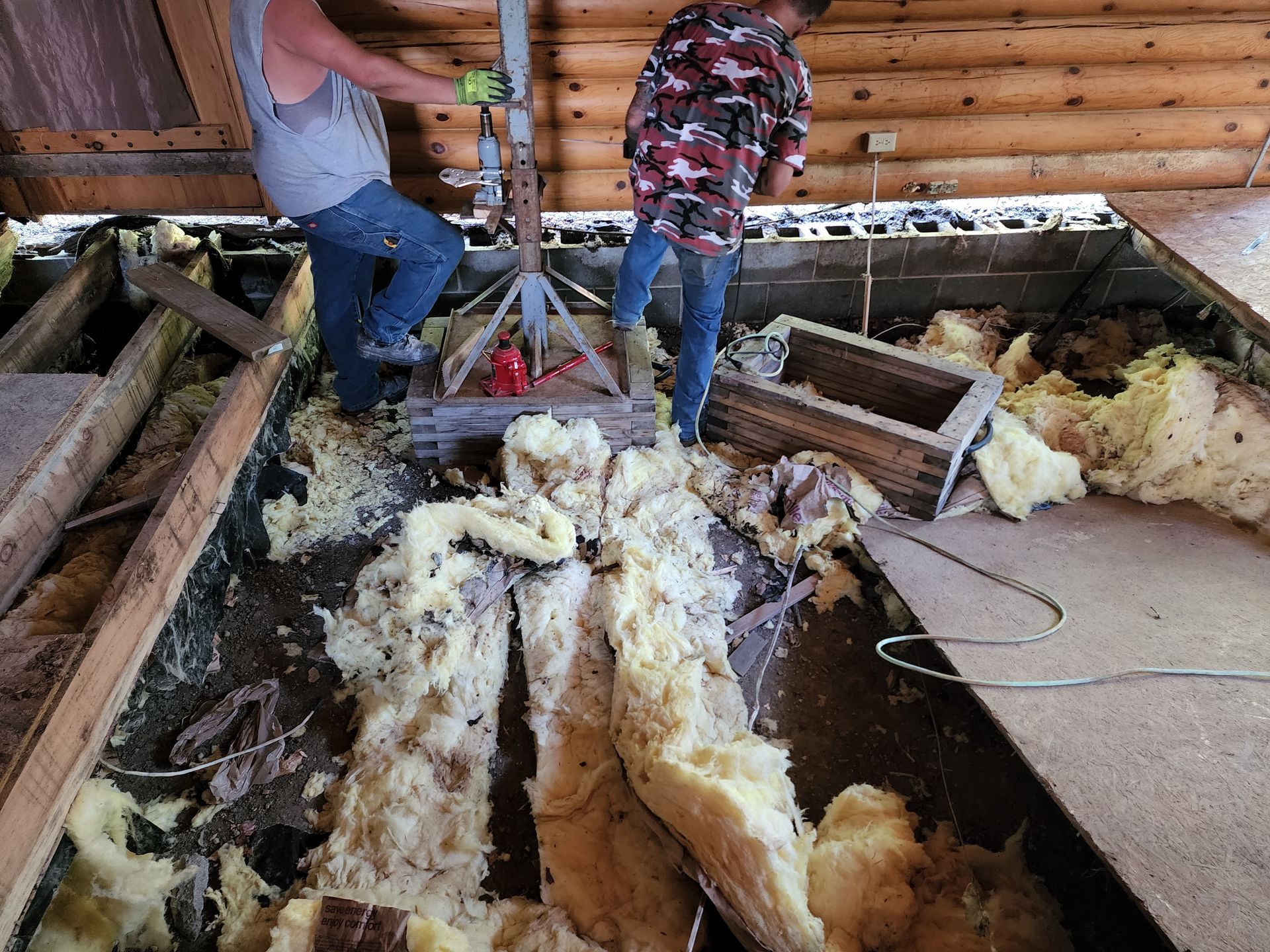Two people standing in an attic with exposed insulation and debris on the floor