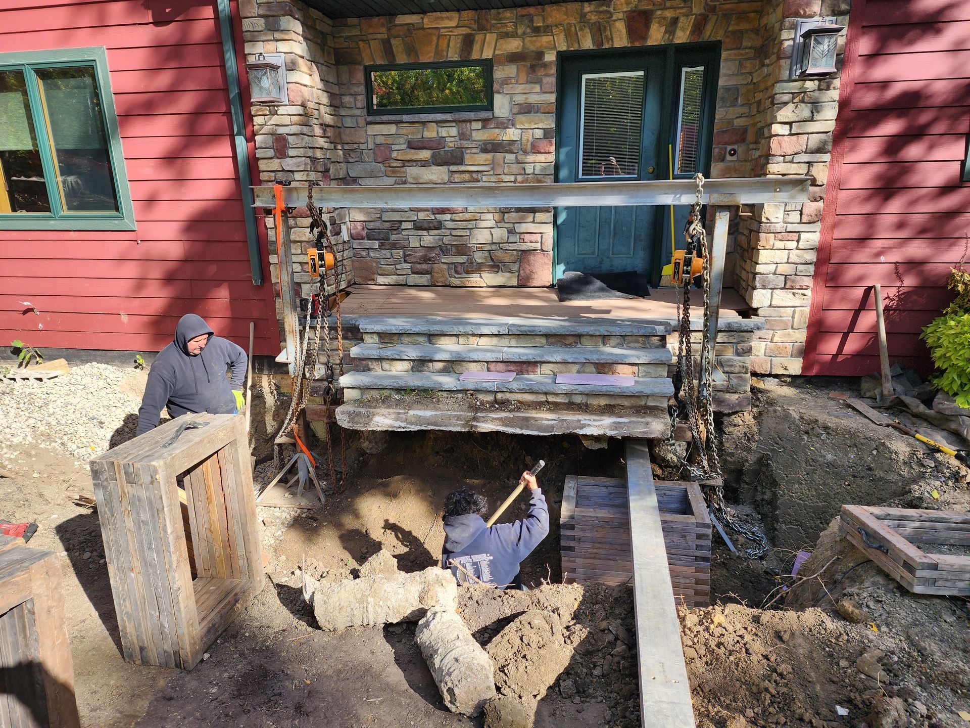 Two workers repairing a front porch and steps on a red house with stone siding