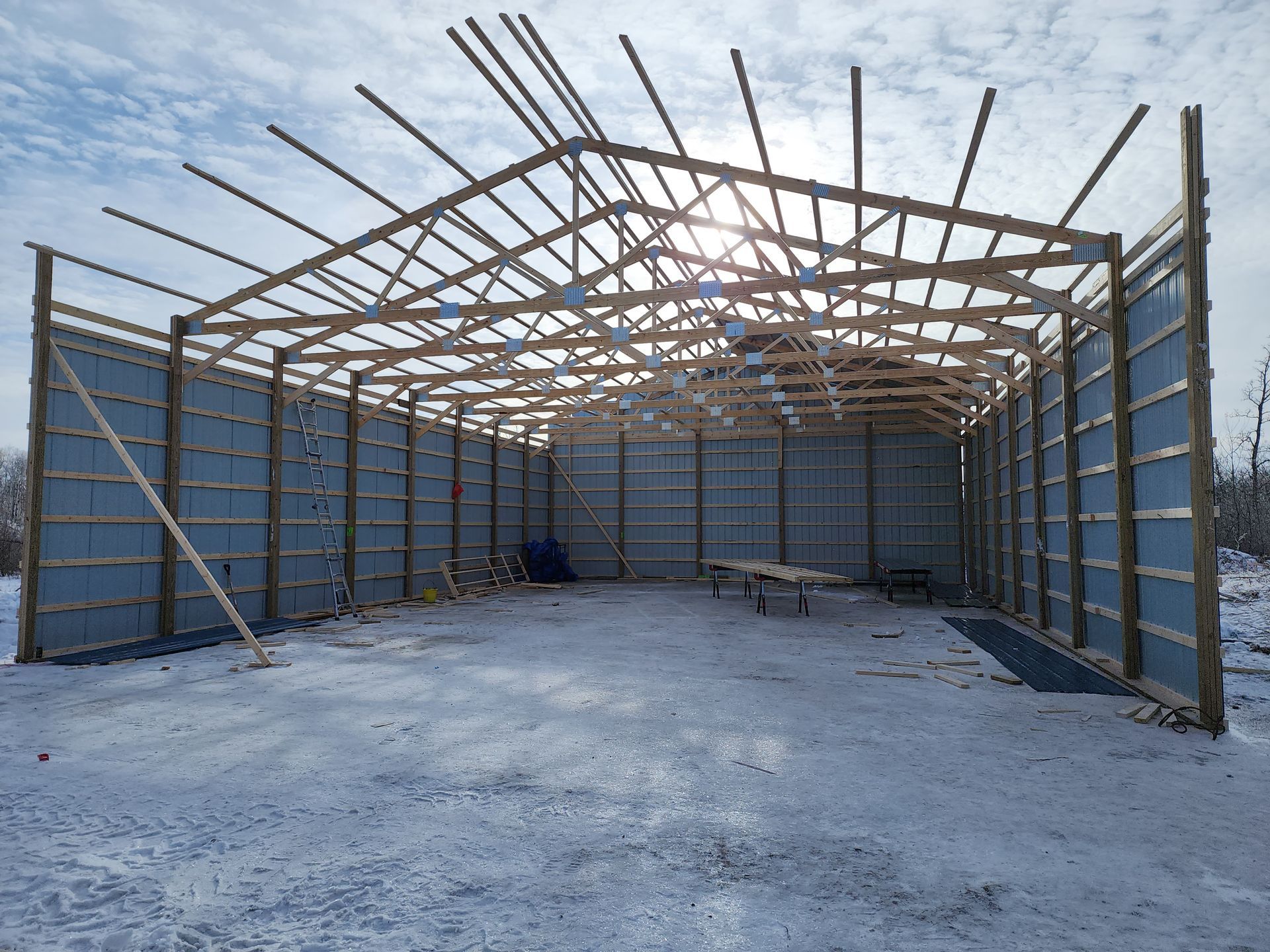 Partially built warehouse frame with metal walls and exposed roof beams on a concrete floor