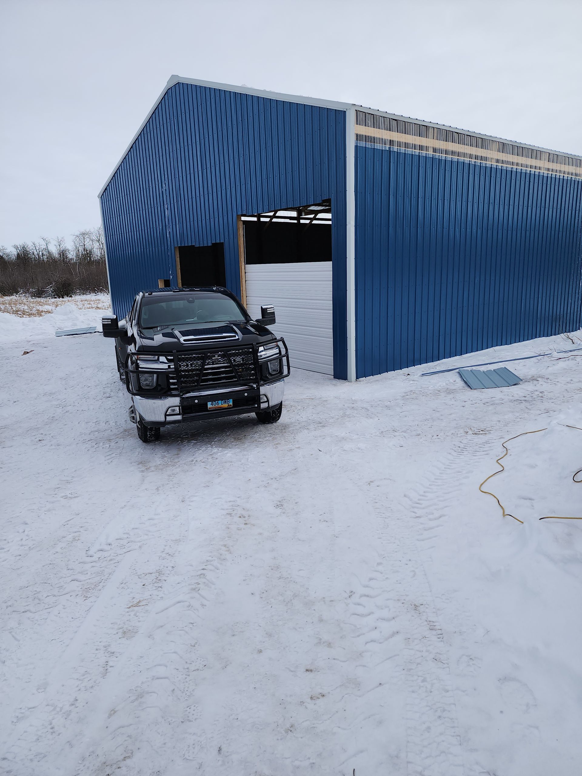 Black truck beside a blue metal shed on a snowy road