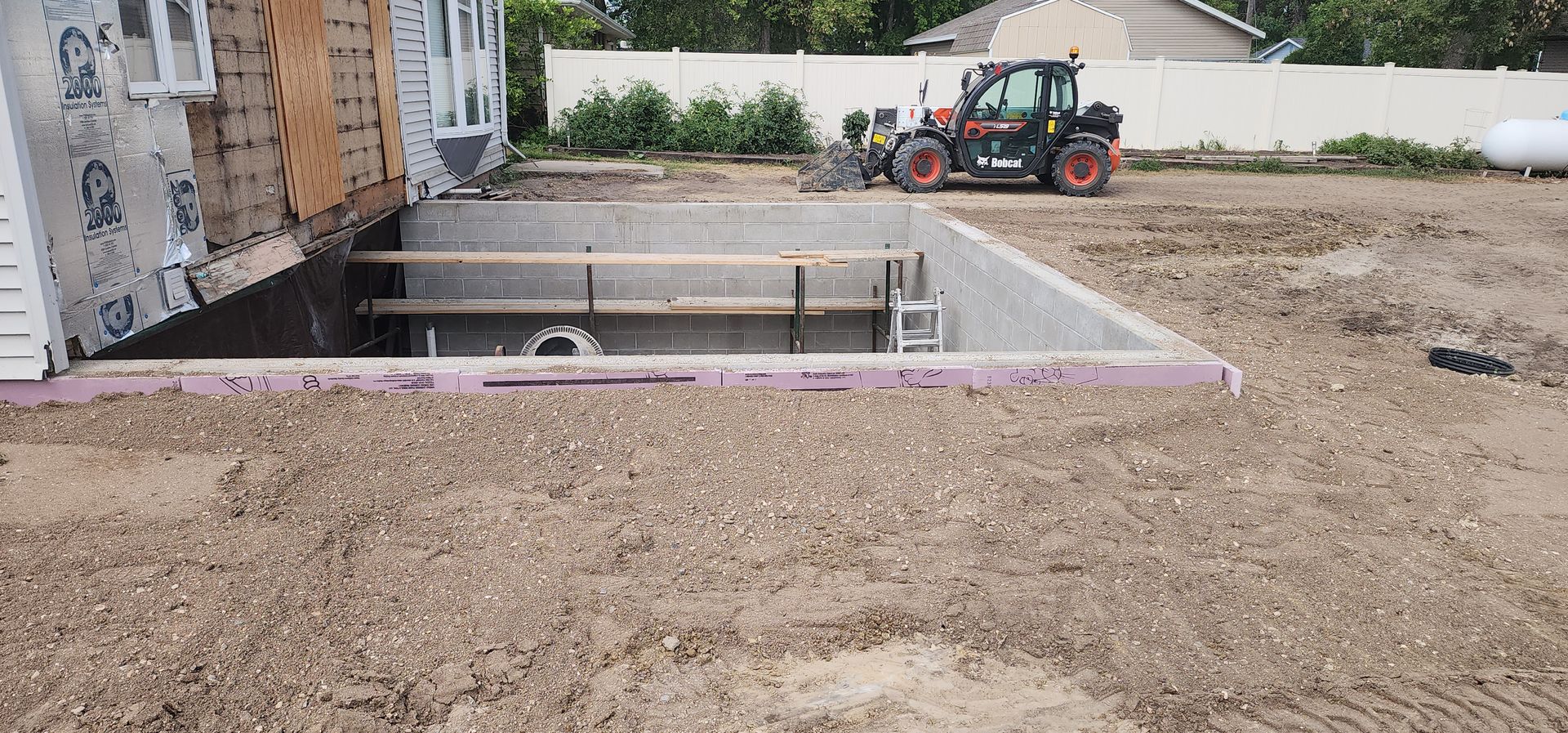 Partially built backyard pool beside a house, with a tractor and dirt grading in the background