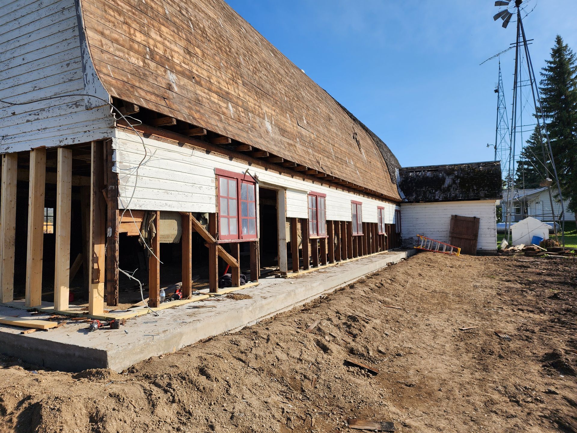Renovated white barn with exposed framing and a dirt lot under a clear blue sky