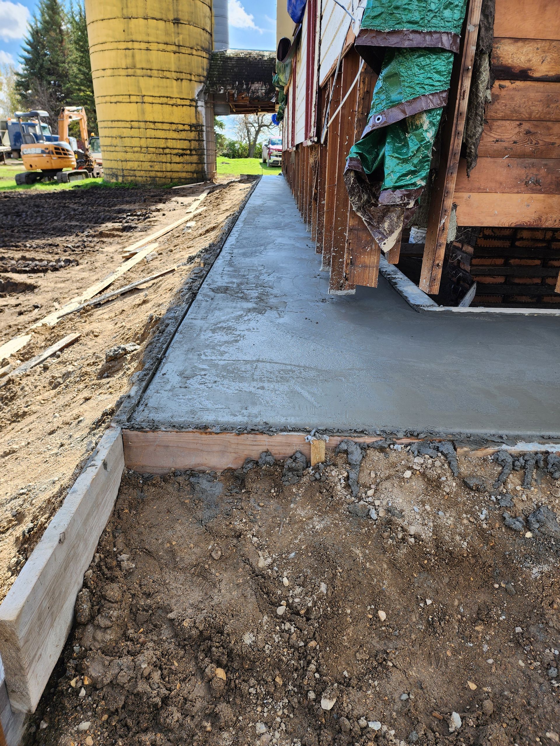 Fresh concrete walkway beside a house under construction, with dirt and construction materials nearby