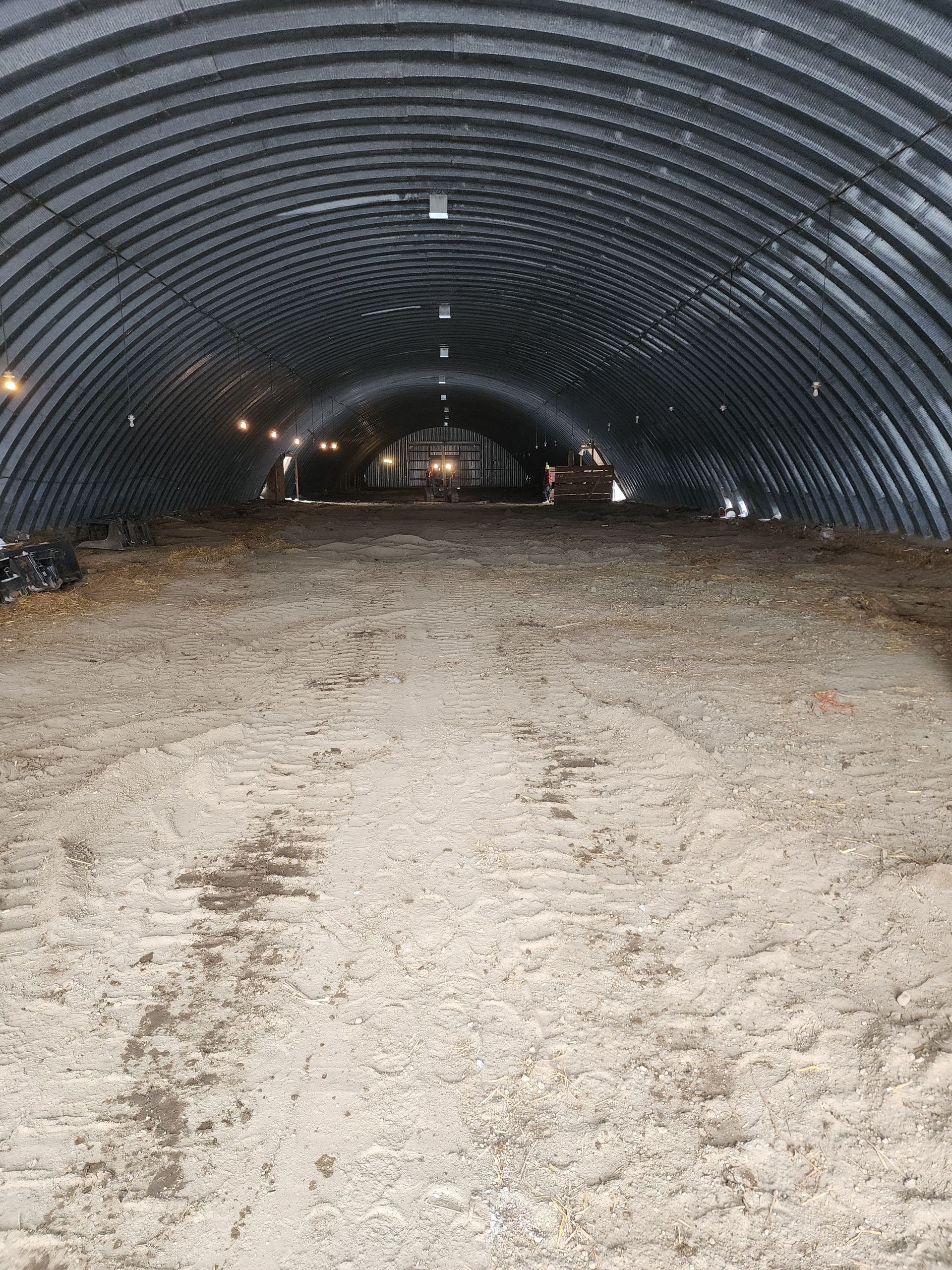 Empty corrugated metal tunnel with a gravel floor and dim lights receding into the distance