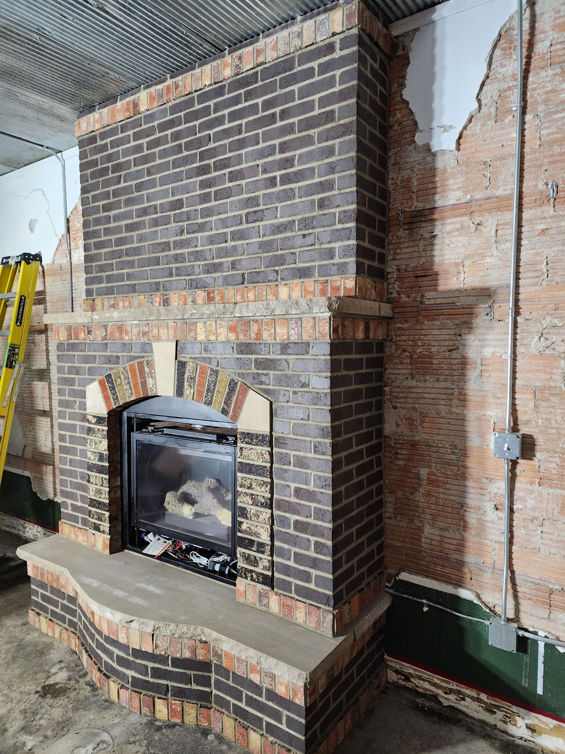 Brick fireplace under construction in an unfinished interior with exposed wall framing and materials.