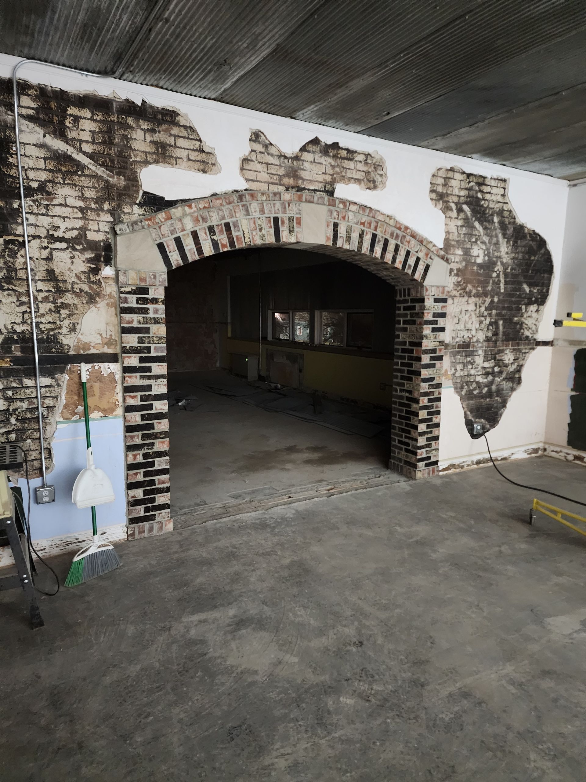 Painted brick archway opening into a dim industrial interior, with worn concrete floor and whitewashed wall.