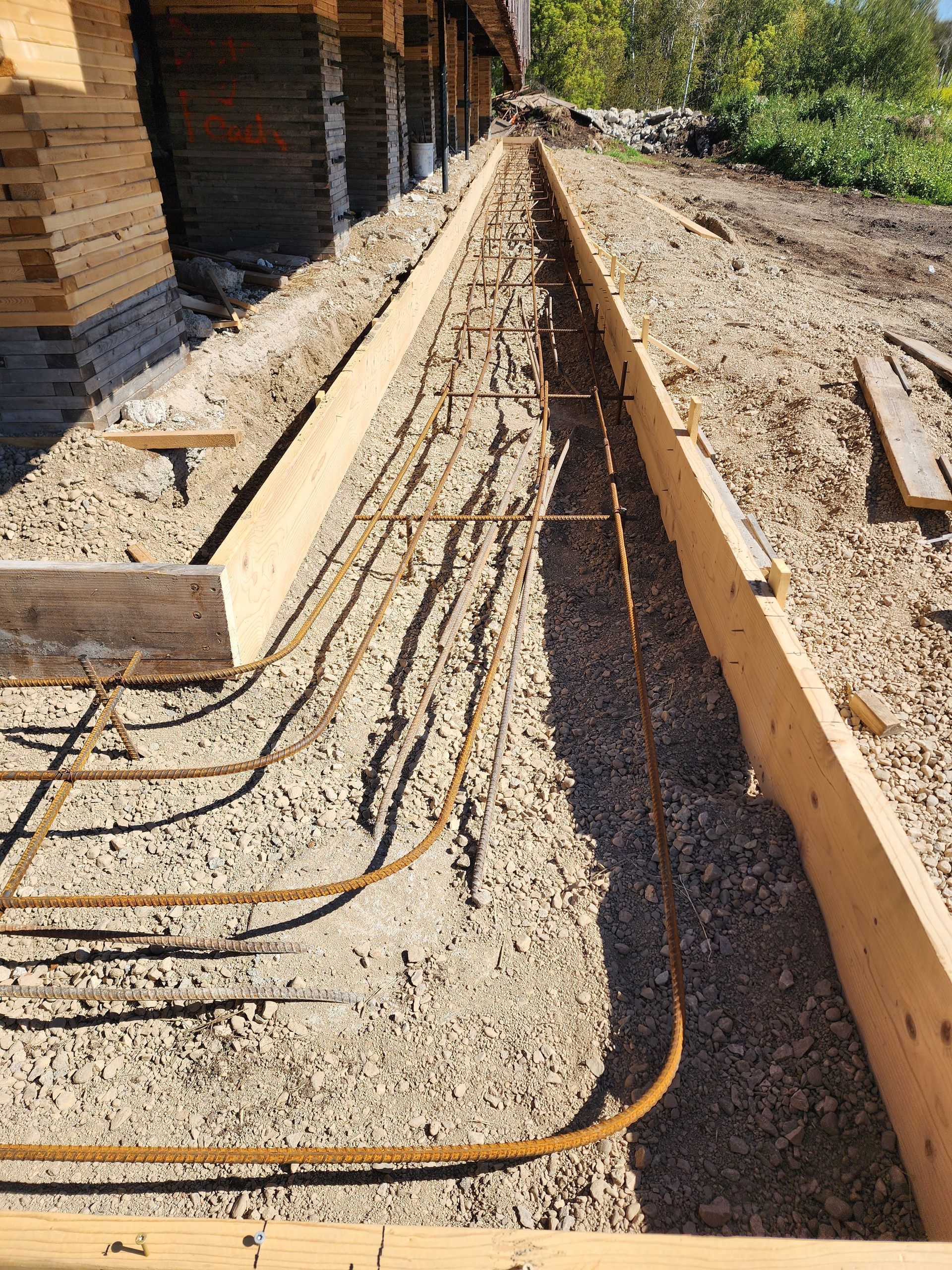 Trench with exposed black cables beside a wooden building on a dirt construction site