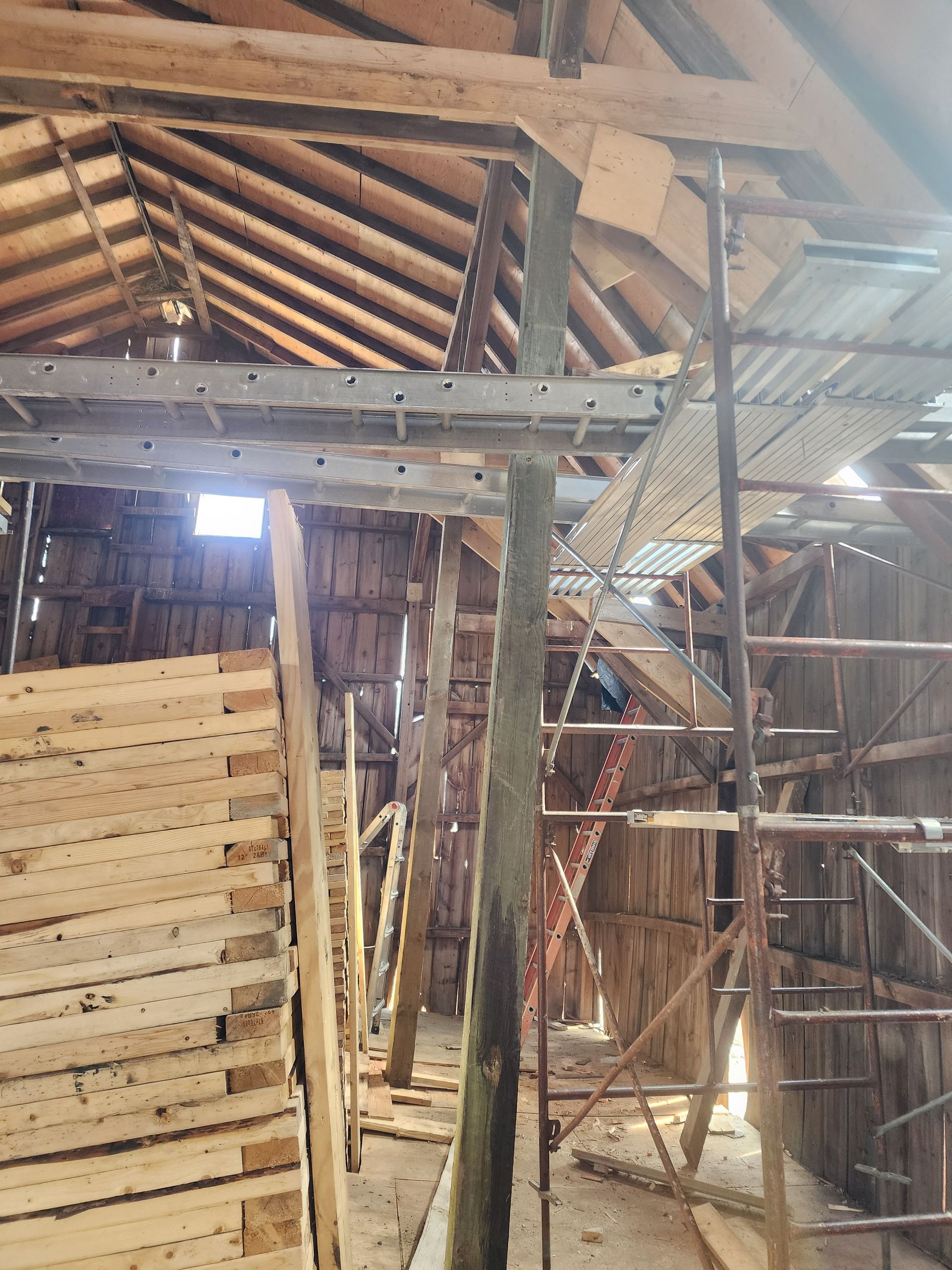 Wooden barn interior with scaffolding and exposed rafters under construction.