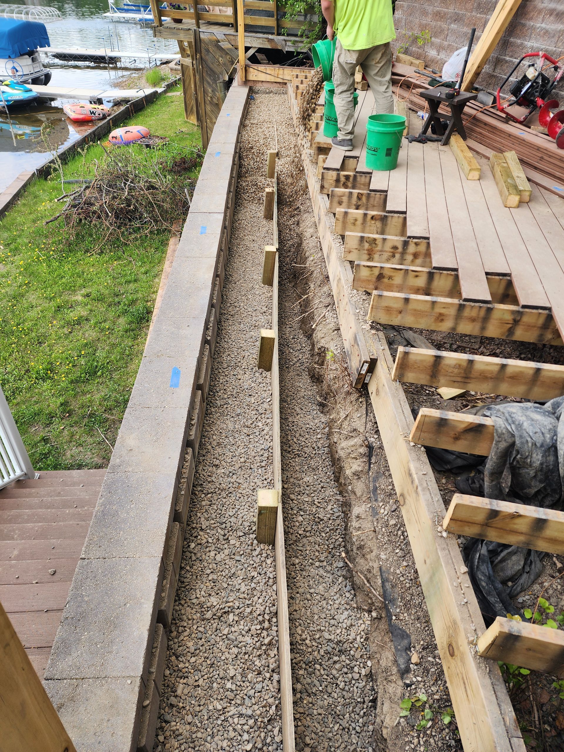 Long concrete trench under construction beside a walkway, with wooden forms and workers nearby
