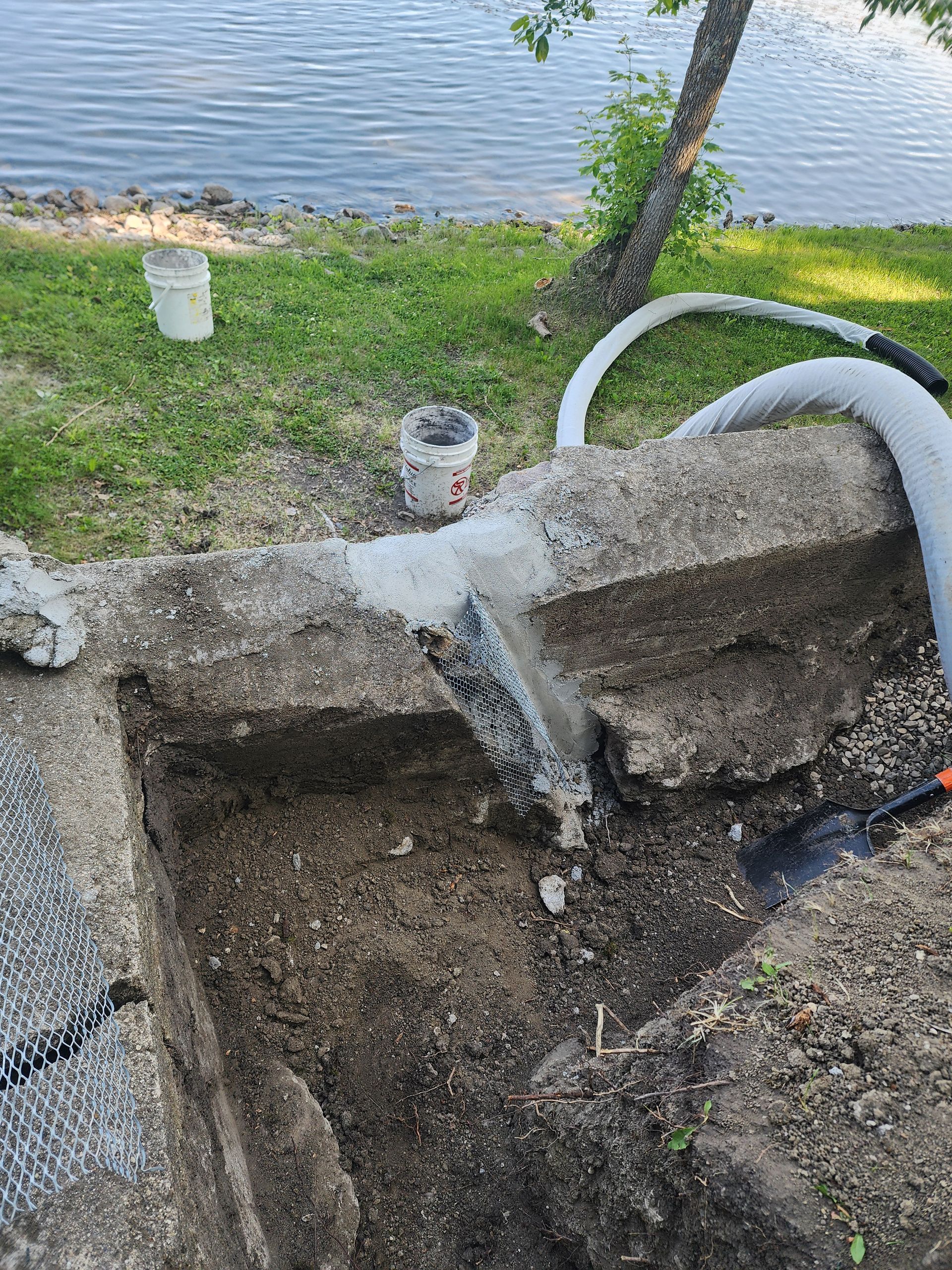 Collapsed concrete drainage hole beside a grassy riverbank, with water flowing into it