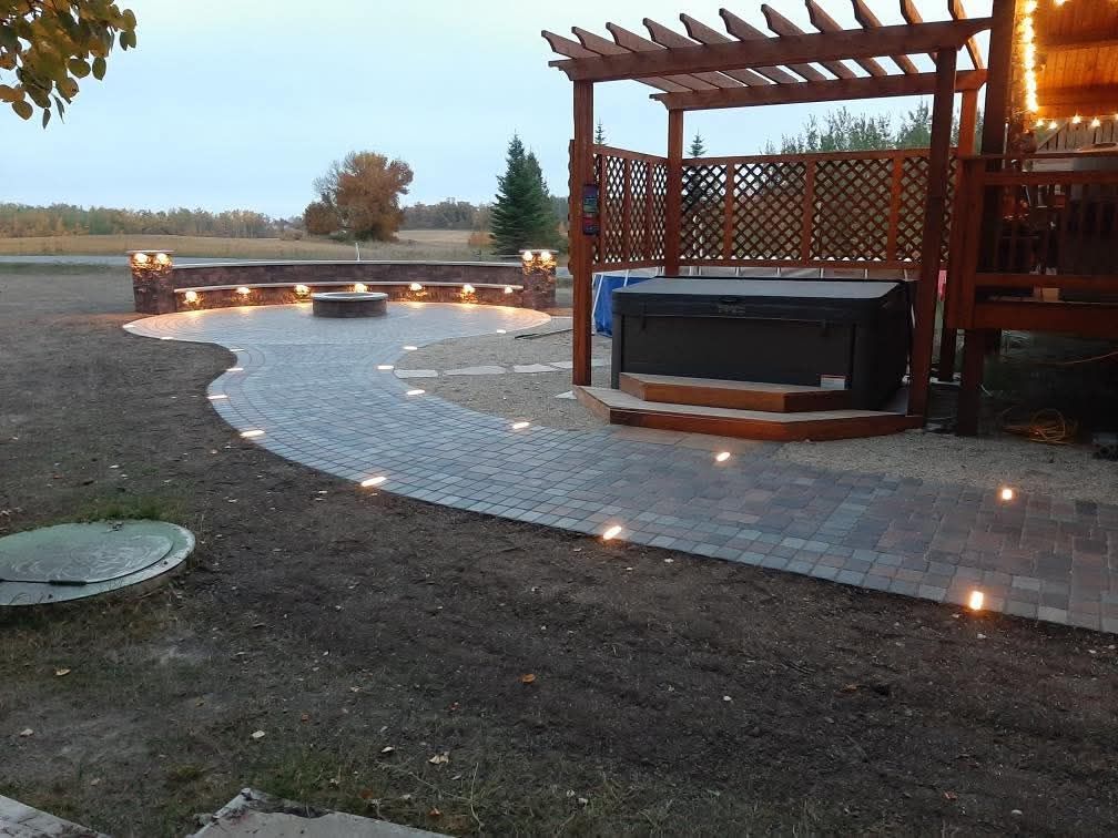 Outdoor patio with lit stone walkway, pergola, and hot tub at dusk.