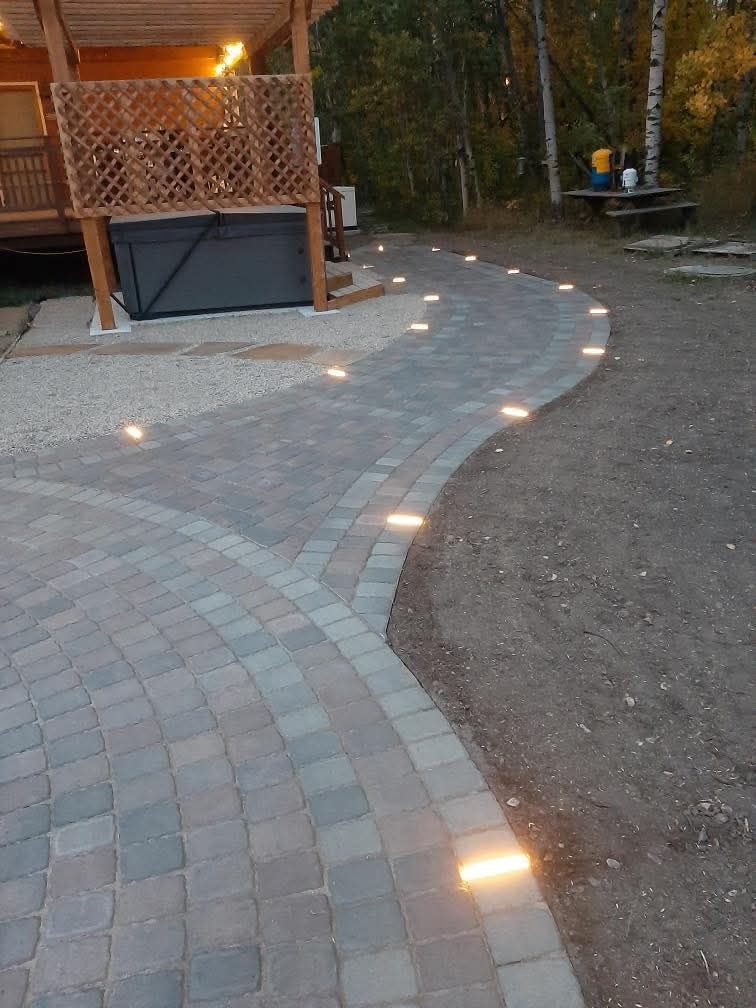Curved brick patio path with glowing ground lights beside a wooden gazebo at dusk