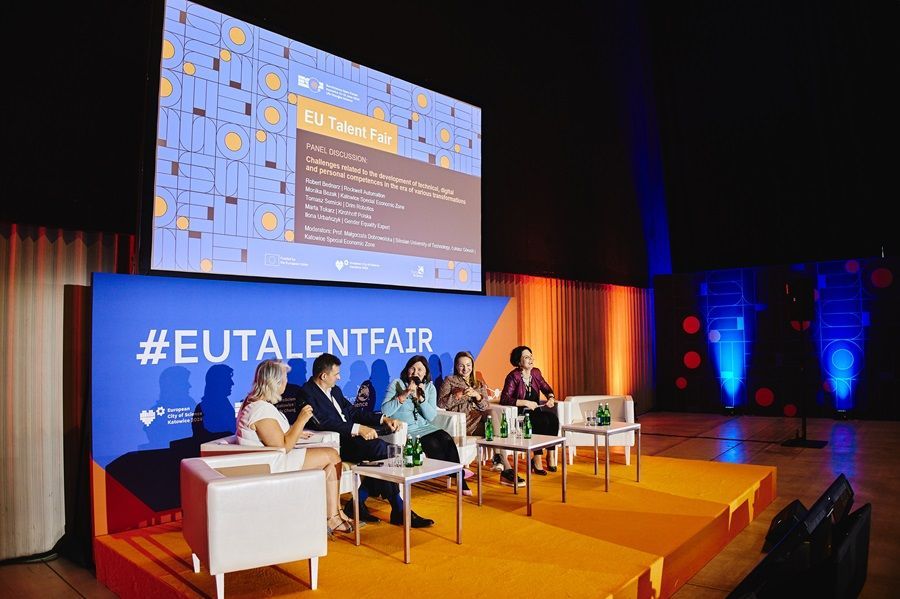 A group of people are sitting on a stage in front of a large screen.