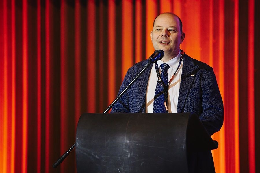 A man in a suit and tie is standing at a podium speaking into a microphone.
