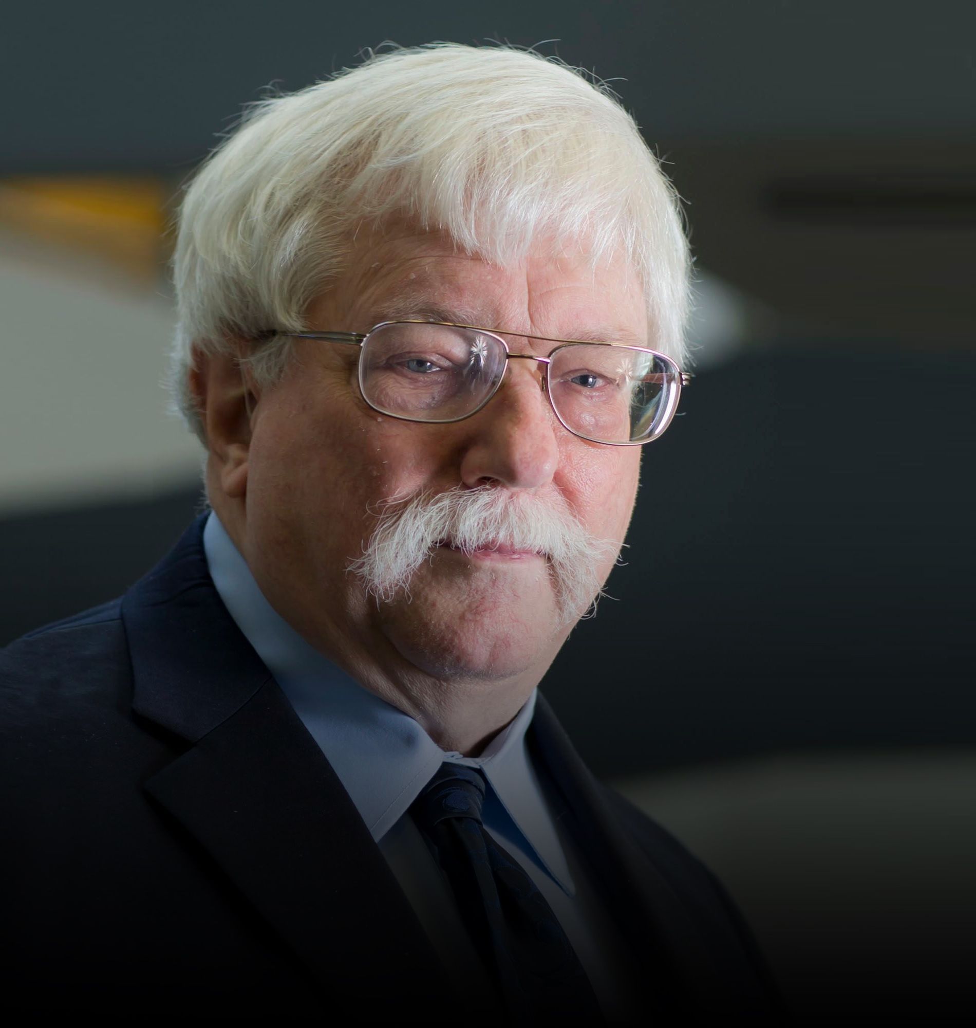 A man with glasses and a mustache is wearing a suit and tie