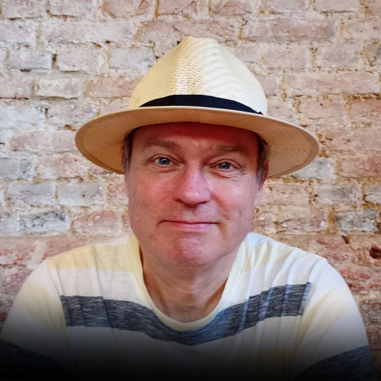 A man wearing a hat is sitting in front of a brick wall