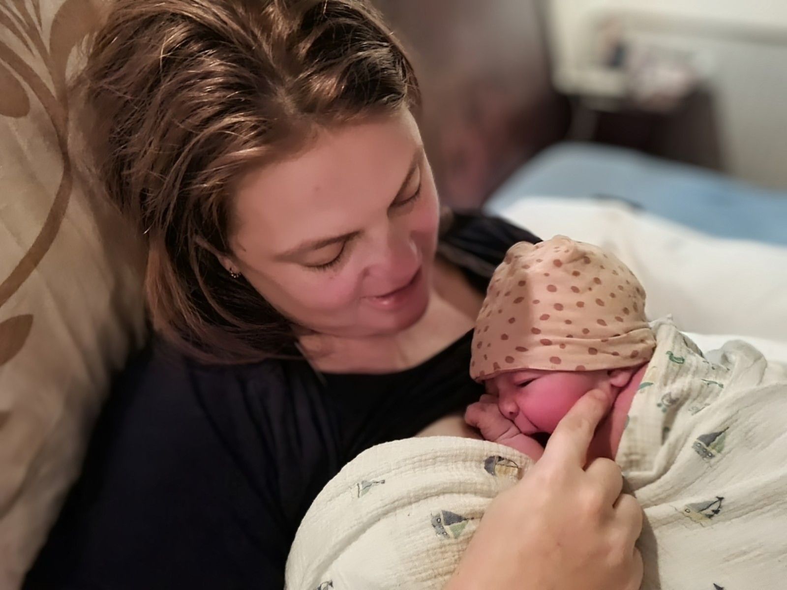 Vrouw houdt een pasgeboren baby in een dekentje in haar armen en kijkt glimlachend naar de baby in een ziekenhuisbed