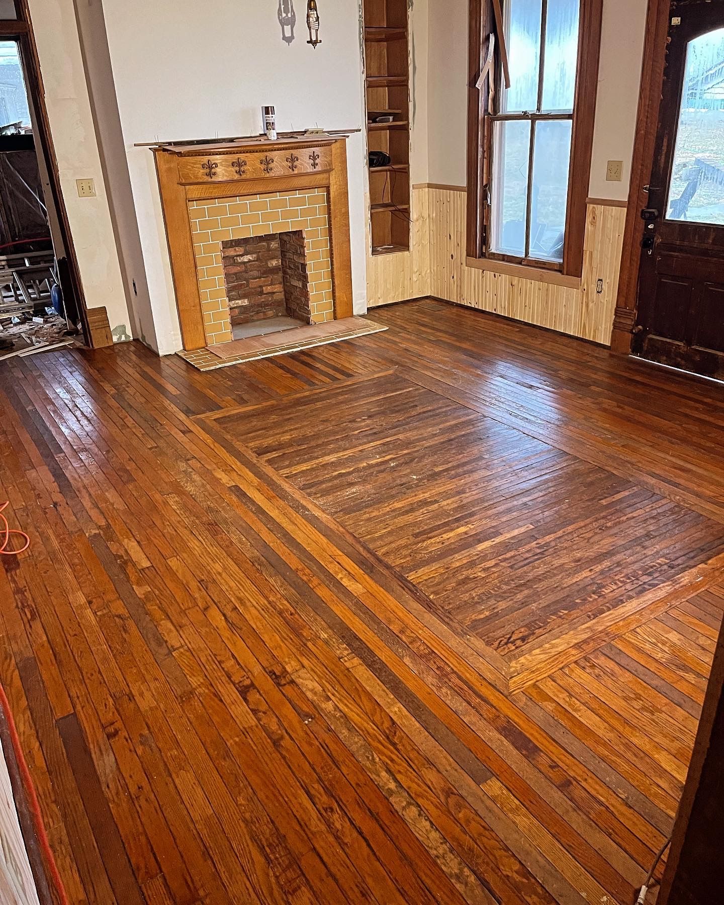 Empty room with glossy hardwood floors, a fireplace, and tall windows with curtains.
