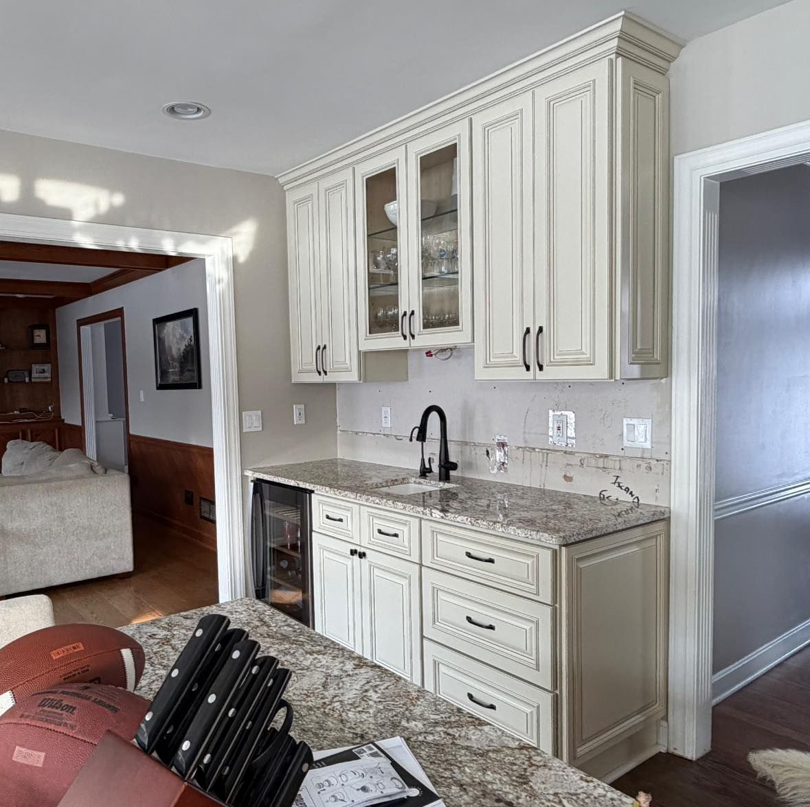 Elegant kitchen wet bar with white cabinets, granite countertop, and sink in a bright open living space