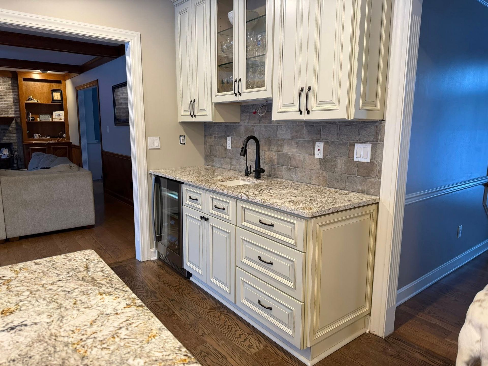 Bright kitchen with white cabinets, granite countertops, black sink faucet, and hardwood floors, opening to a living room
