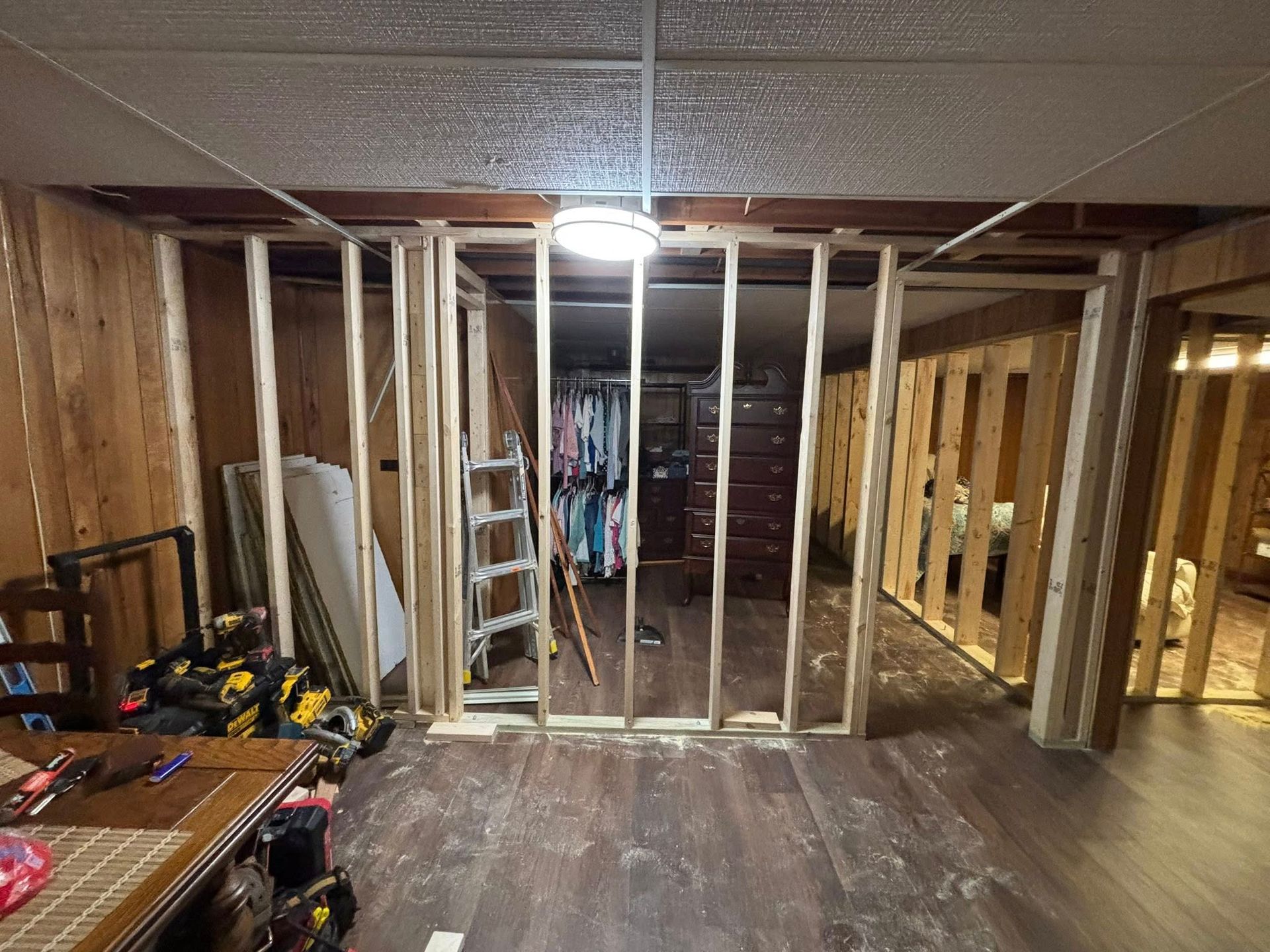 Basement room under construction with exposed wall studs, ladder, tools, and unfinished flooring.