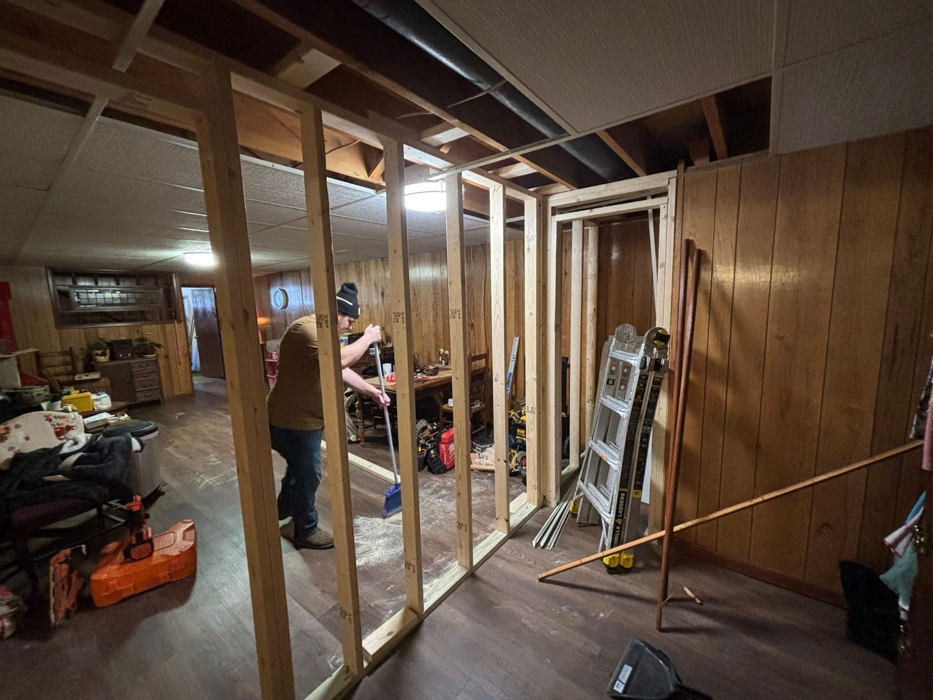 Partially framed basement renovation with two workers and ladders under exposed ceiling beams