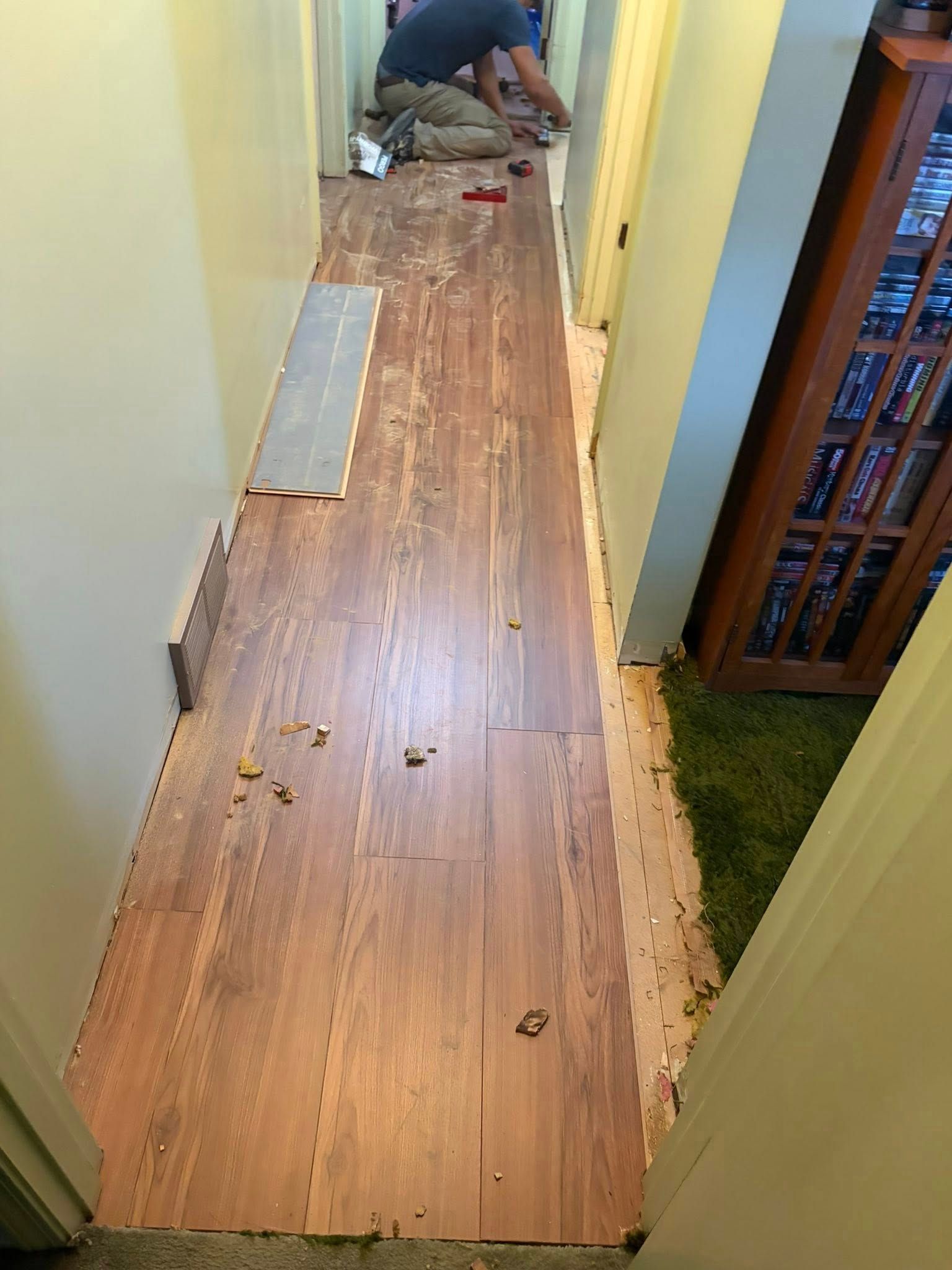 Narrow hallway with damaged wood flooring being repaired; worker crouches at the far end.