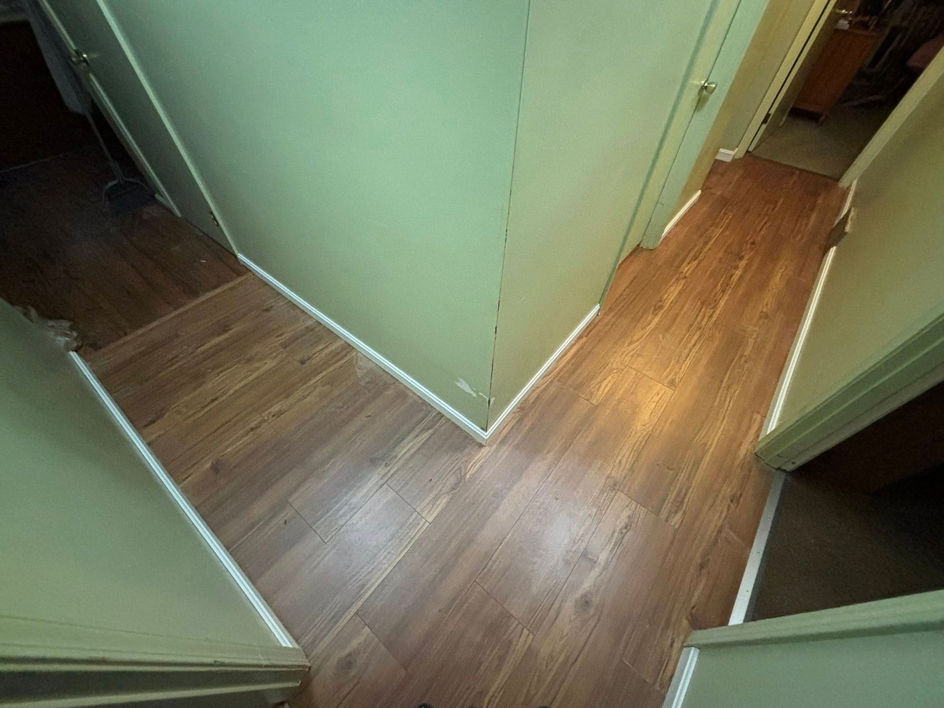Narrow wooden hallway with mint-green walls and a dark floor, viewed from above.