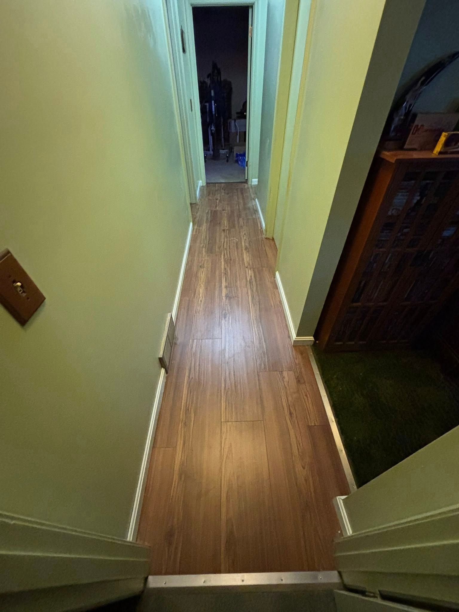 Narrow hallway with wood floor and pale walls, leading to a dark doorway at the end.