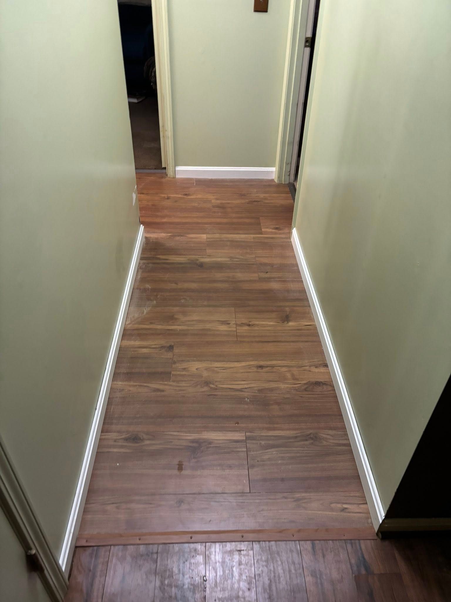 Narrow hallway with wood flooring and light walls, lit by LED strip lights along both sides.