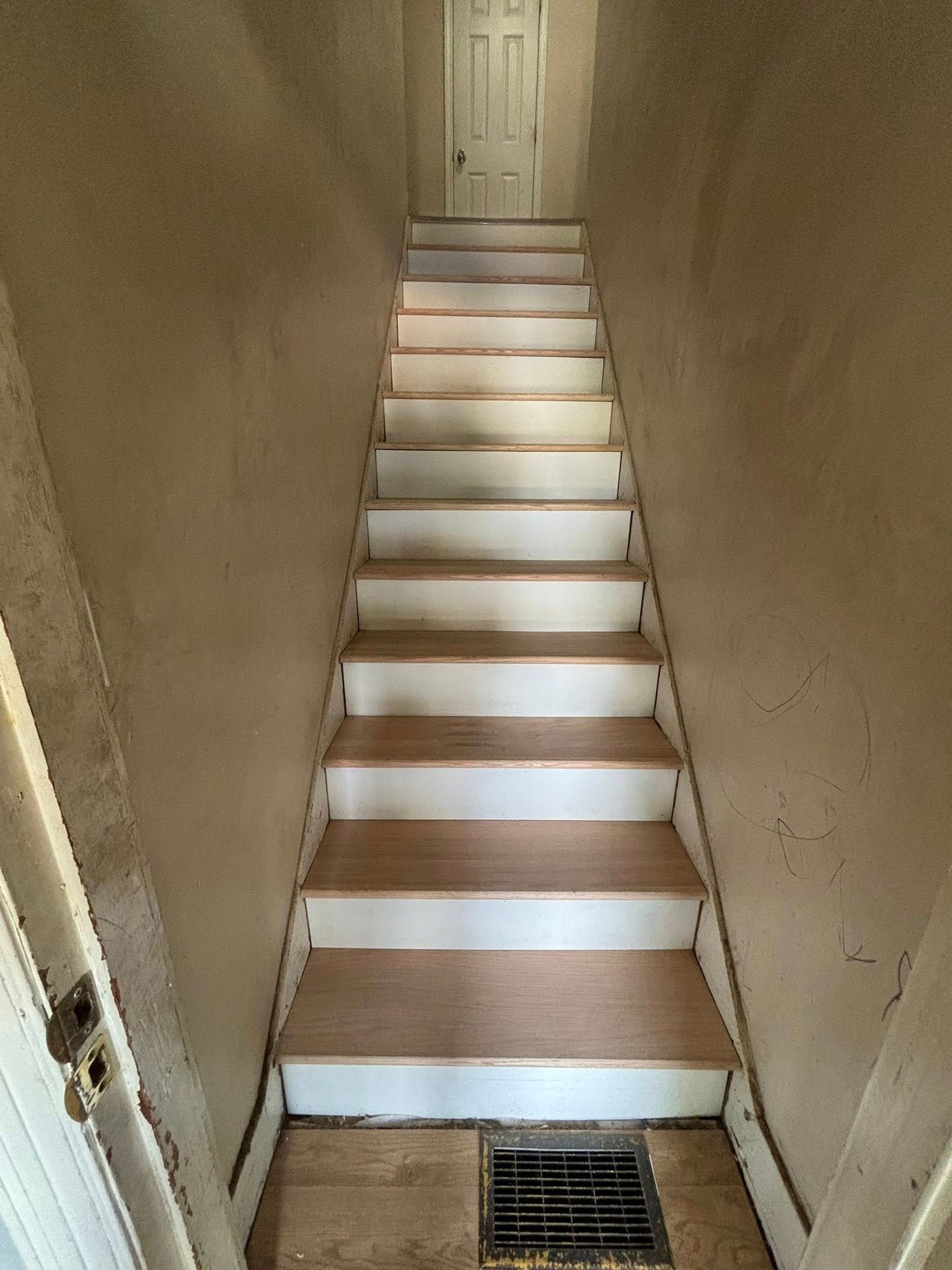 Narrow indoor staircase with white steps and a door at the top, viewed from below.