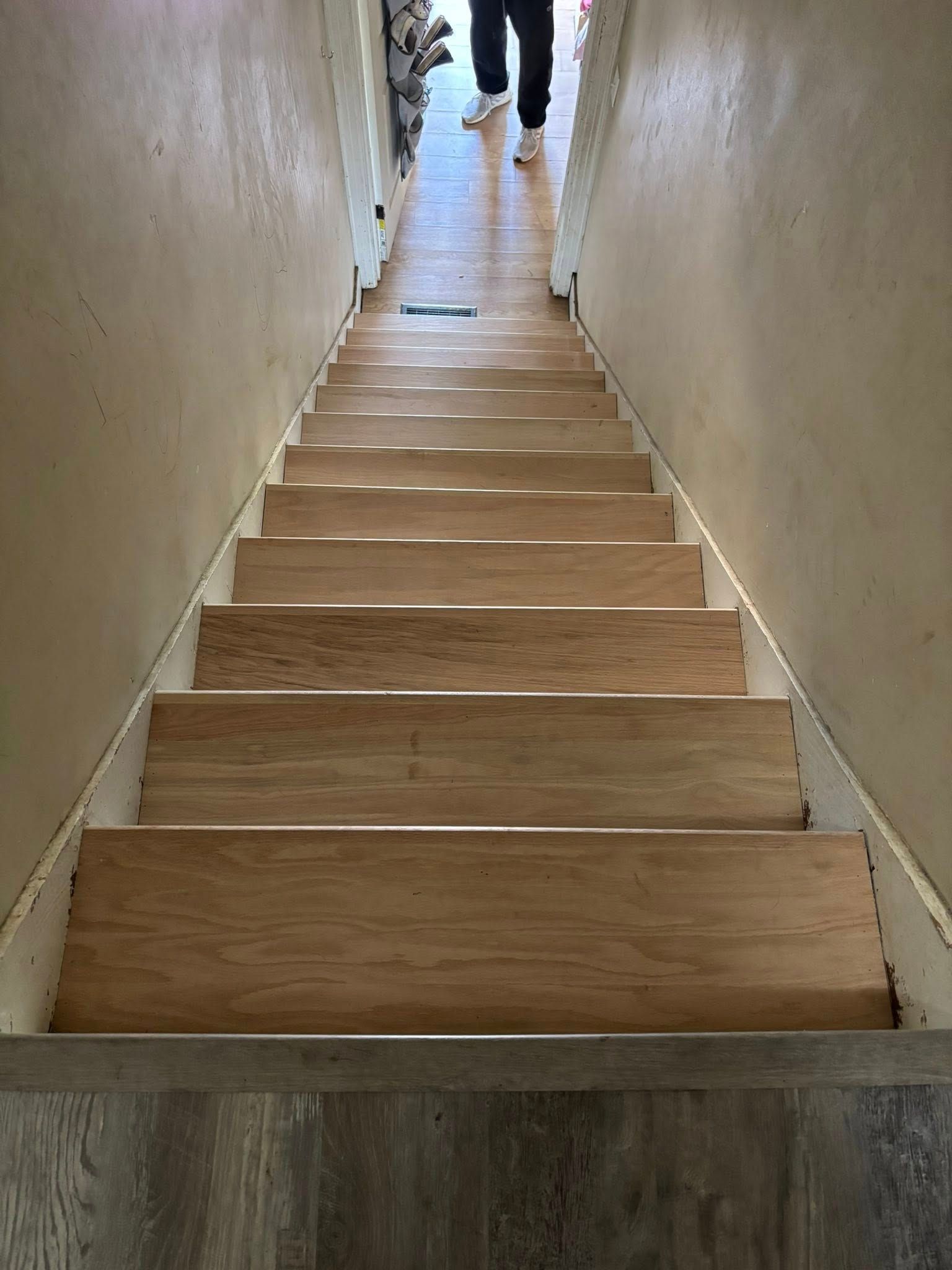 Wooden staircase between beige walls, with a person standing at the top landing